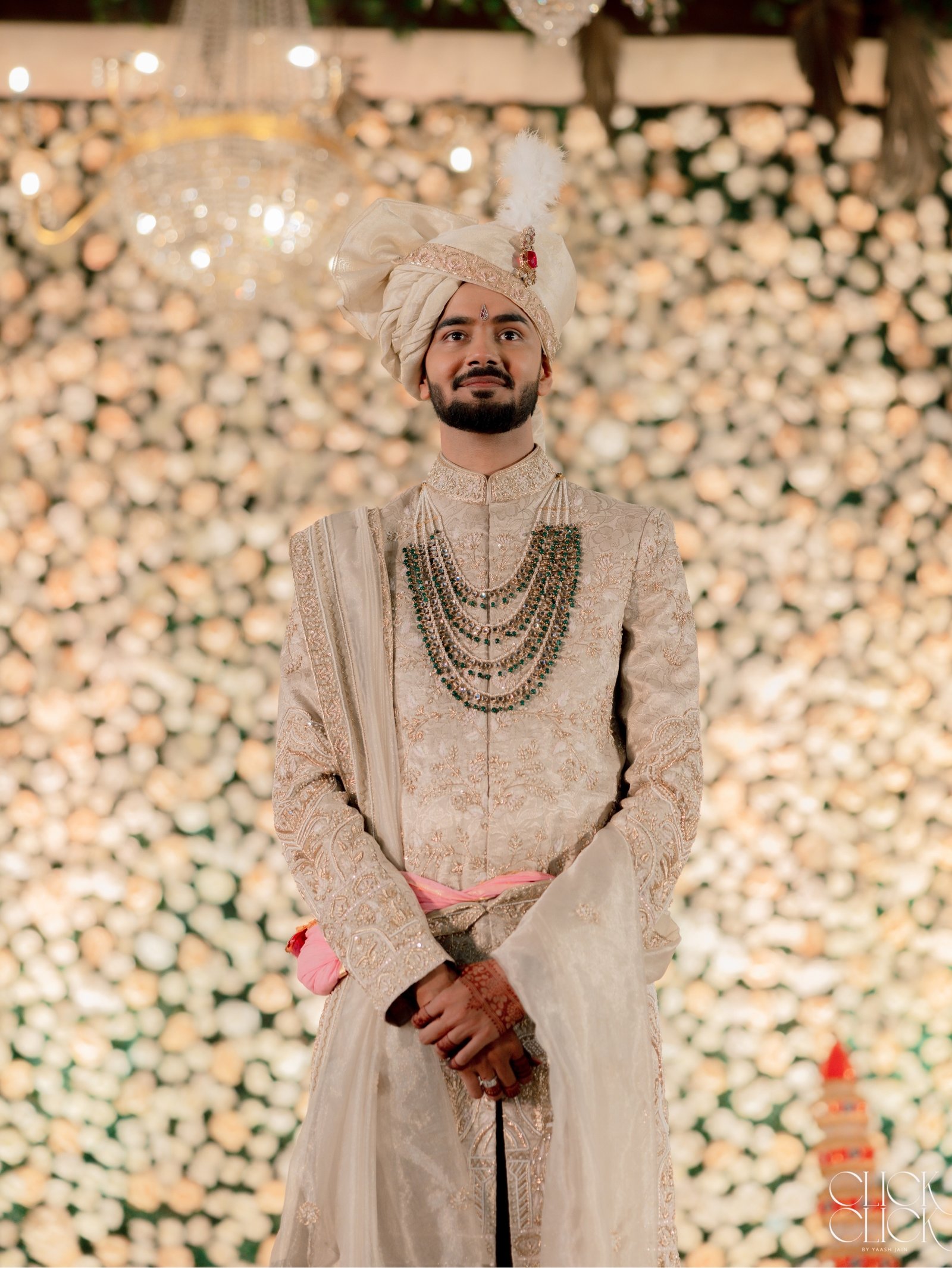 A groom standing before a softly lit wall of flowers